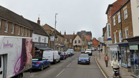 High Street in Oakham is pictured. It is a busy street lined with shops and homes, with cars parked along the left lane.