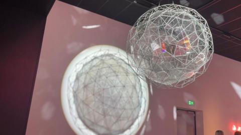 One of the features of the exhibition. A poloygonal sphere - if you can still call it a sphere- is suspended from the ceiling. It seems to be made from some kind of wire and glass combination. A light is being shone through it, which creates a geometric pattern on the wall of the darkened room.