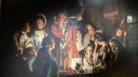 A painting by Derby Artist Joseph Wright features a group of people lit by candelight looking at an experiment on a bird in an air pump. 