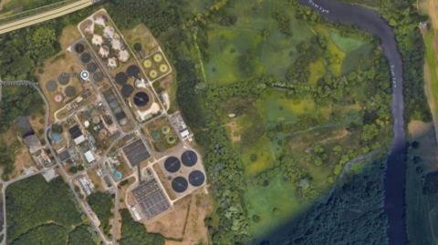 An aeriel view of sewage and water treatment works at Whitlingham, in the south of Norwich. The River Yare can be seen running close by with green fields and trees in between.