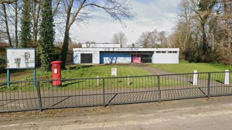 Bookham Community Centre on 164 Lower Road. There is a black fence and an area of green grass in front of the white building, with trees either side. 