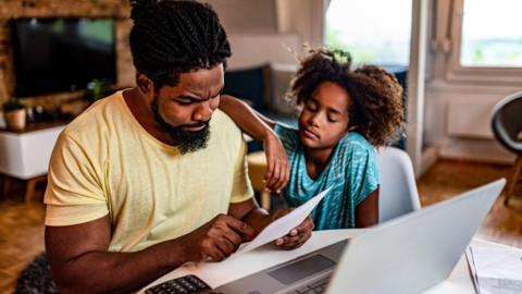 A father and his young daughter look worried whilst looking at bills