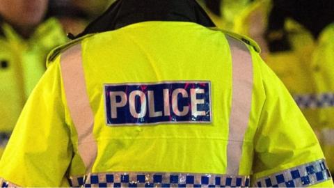 Generic image of a police officer in Greater Manchester, wearing a hi-vis yellow jacket with police labelled on the back.