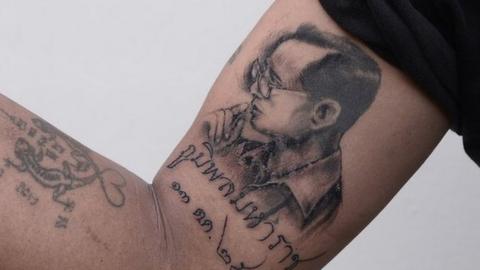 A man flexes his arm showing a portrait tattoo of King Bhumibol