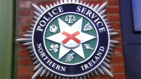 A PSNI crest on a red-brick wall