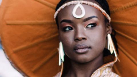 A woman wears a large circular headpiece. The underside is a burnt orange colour.