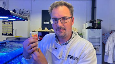 Professor Michael Sweet holds a tube of the new coral-friendly sunscreen