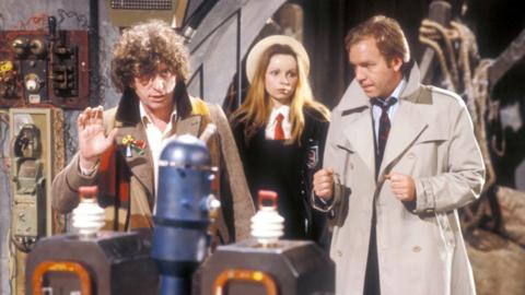 Tom Baker as Doctor Who stood with Lalla Ward as Romana behind him and Tom Chadbon as Duggan on the opposite side of the frame