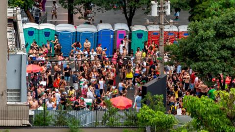 A crowd of people outside portable toilets at a festival.