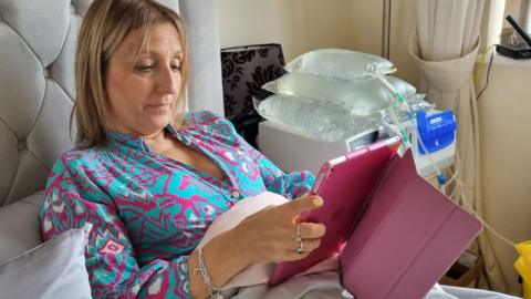 Image of a woman in bed reading while connected to a dialysis machine