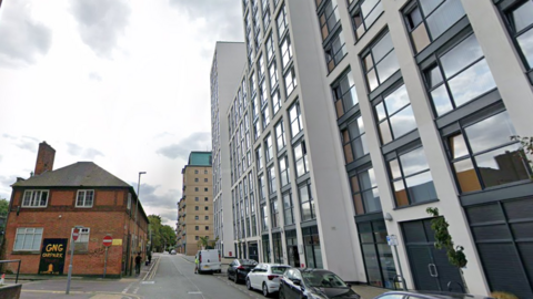 A back street in Leicester with looming blocks of flats on one side of the road