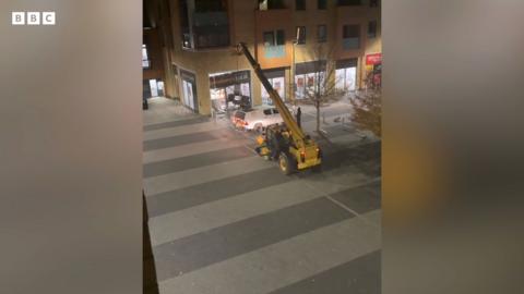 Phone footage from window shows yellow telehandler in middle of street pulling cash machine from Sainsburys