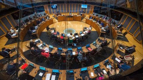 A general view of the Senedd debating chamber seen from above. Eluned Morgan is stood addressing the Welsh Parliament.