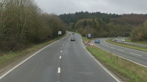 A road with two lanes, turning into three lanes, beside a grass verge, with two further roads beyond