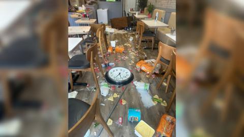 Food and drink tipped on the floor of the cafe and mess everywhere. A wall clock has also been put on the floor.