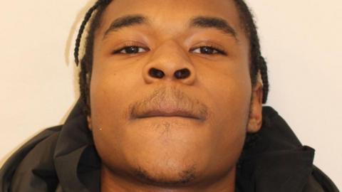 A custody photo of Gabriel Charles who is wearing a black padded jacket looking directly at the camera against a plain light background.