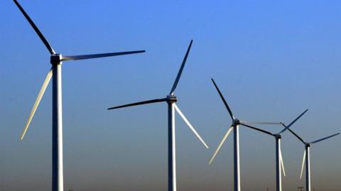 A view of wind turbines against a clear blue sky. The blades of the turbine are white.