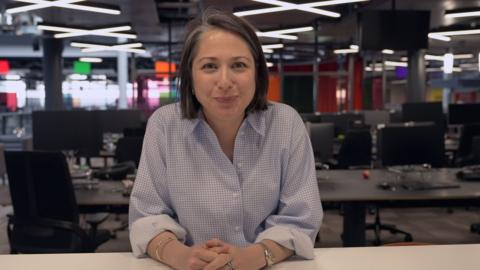 Teleri Glyn Jones in a button up shirt at a desk in front of computer screens