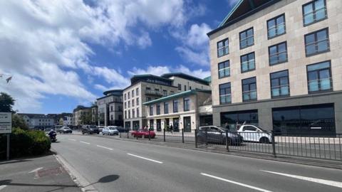 A series glass and limestone finance buildings, next to a wide road, leading up to a roundabout.