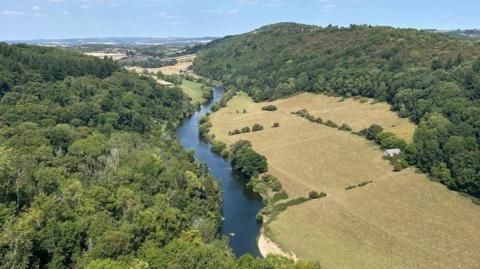 A wooded and green valley with a river going through the centre.