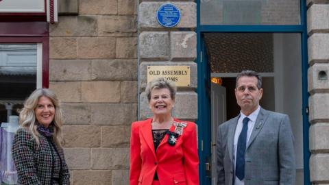 Beryl Anderson Sue Snowdon and Sam air in front of plaque