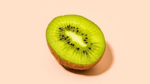 Half a kiwi sliced length ways on a pale orange background