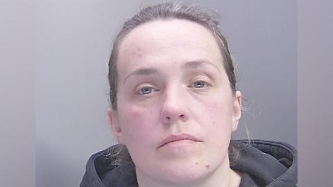 Modesta Kelpsaite in a police custody shot looking at the camera. She has brown hair which is pulled back and is wearing a dark-coloured hooded top.