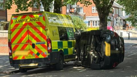 An overturned car next to an ambulance in the aftermath of a collision in Blackbird Road, Leicester.