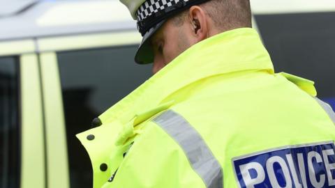 A policeman wearing a police jacket standing next to a police car