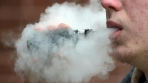 A closeup of a man vaping with a plume of smoke around his mouth.