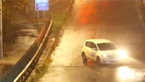 A white car performs a U-turn on the Humber Bridge and is facing into oncoming traffic. The footage has been captured at night and the road is illuminated by street lights. 