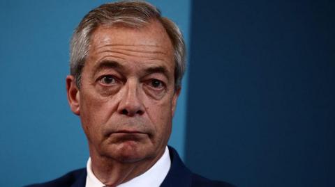 A close up of a man with grey hair and a suit in front of a blue background