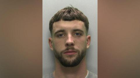 Aidan Cashley pictured wearing a grey sweatshirt. He has a dark brown beard and short, flat brown hair. 