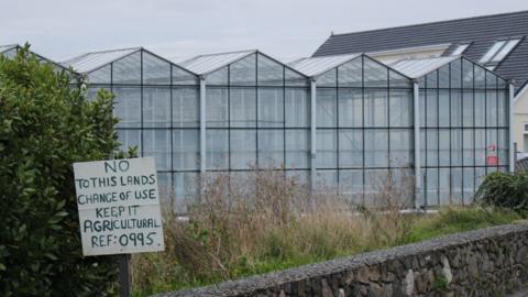 Protest sign in front of abandoned greenhouse.