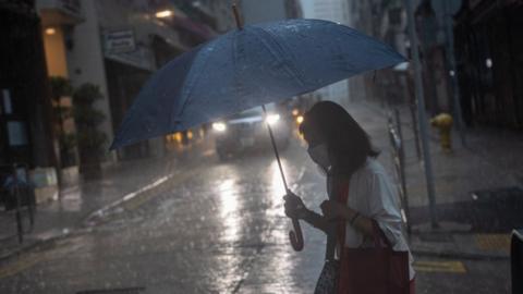 A woman carries an umbrella as she crosses a street during a rain storm in Hong Kong.