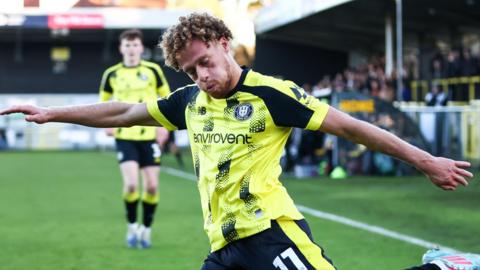 Stephen Duke-McKenna, with arms outstretched and eyes looking down, about to cross the ball for Harrogate