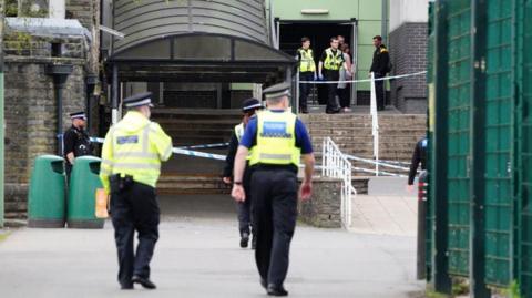 Police stood outside Ysgol Dyffryn Aman in uniform, stood with their backs to the camera.