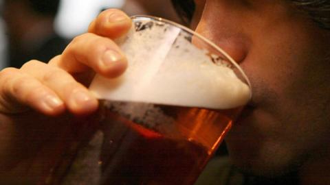 A stock image of a man drinking a pint of beer with a frothy head.