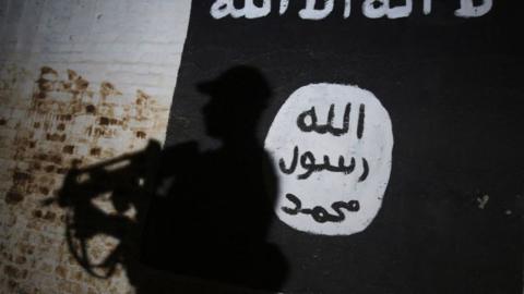 The shadow of an Iraqi soldier is cast over the Islamic State flag