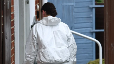 A woman wearing a white forensic suit entering a house by a side door following the attack in Sandown 