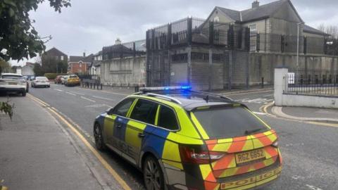 A yellow and blue police car parked outside Strabane police station 