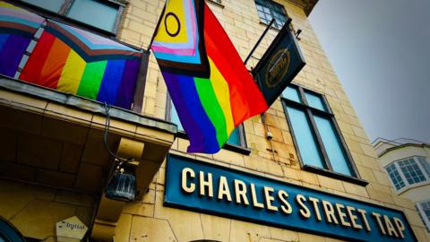 The outside of a pub named Charles Street Tap. There is a LGBTQIA+ flag hanging off the balcony.