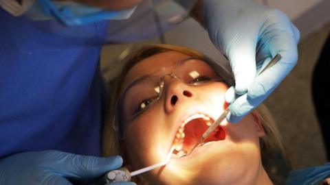 A woman lies back in the dentist chair, having her teeth checked