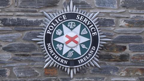 A large Police Service of Northern Ireland crest on a grey stone wall.