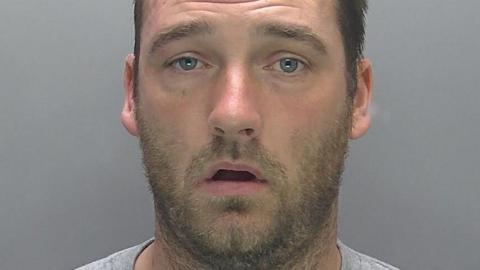 A police mugshot of Barry Thrower, with dark hair and a beard.