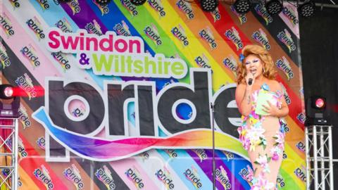 A performer on the Swindon Pride stage set against a colourful backdrop