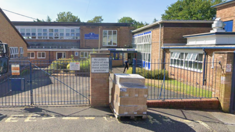 An exterior of a redbrick primary school with blue gates. There is a sign on the gates saying 'no public rights of way exist within these school premises.'