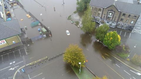 An aerial shot shows a car submerged in floodwater.