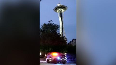 The Seattle space needle in the evening sky. There is a police car in the foreground.