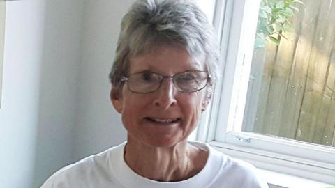 Suzanne Rees, wearing a white t-shirt and black wire glasses smiles in a photo